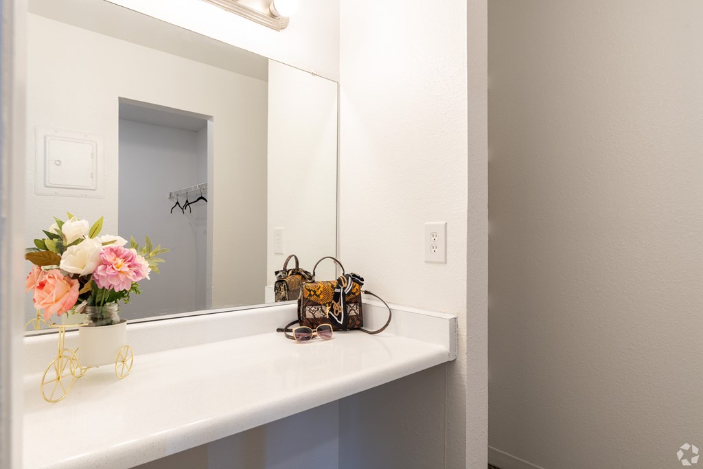 A white bathroom vanity with a mirror, a vase with flowers, a bicycle, and a pair of sunglasses.