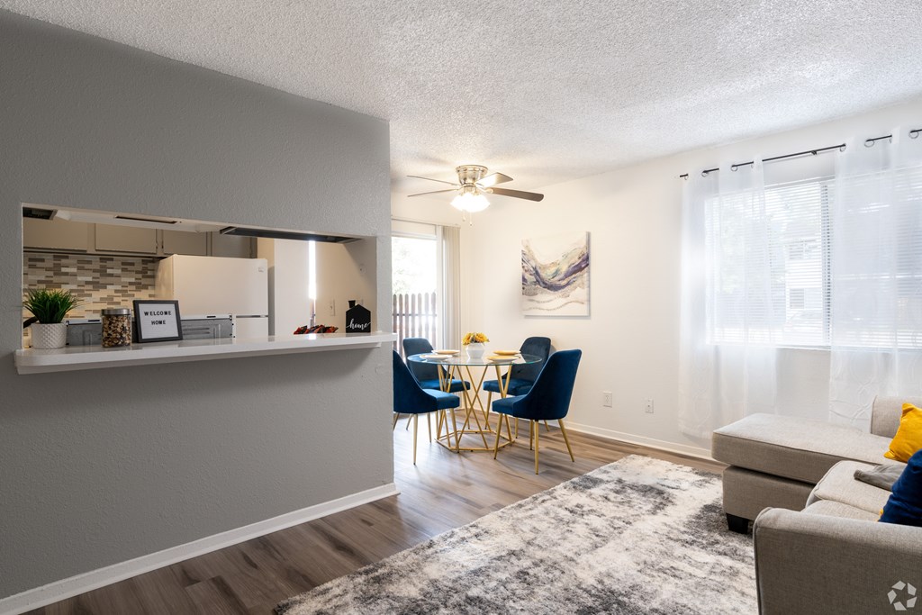 A living room with a grey couch and a dining table with blue chairs.