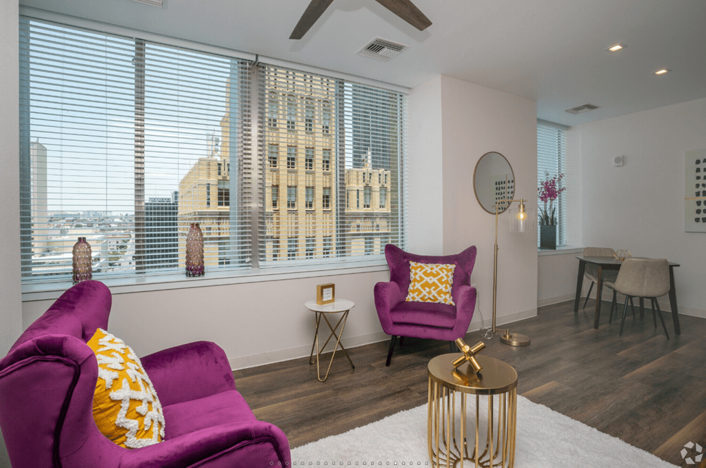 A purple chair with a yellow pillow is in the foreground of a room with a large window.
