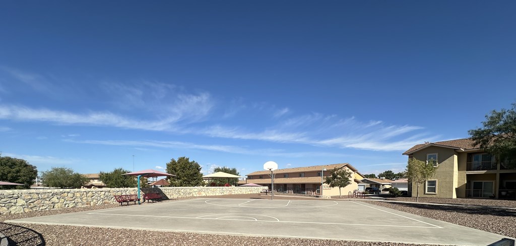 A basketball court is surrounded by a stone wall and buildings.