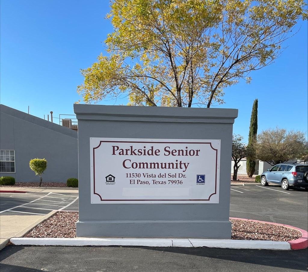 A sign for Parkside Senior Community stands in front of a tree.