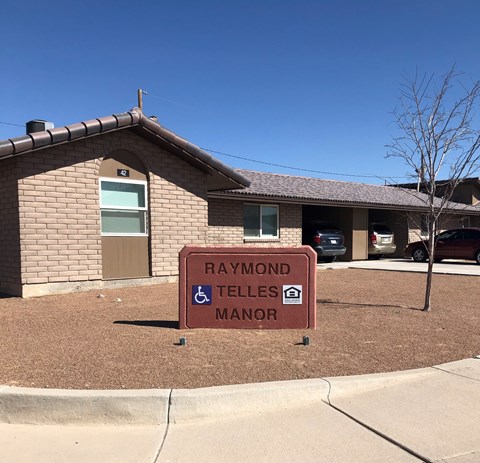 A sign in front of a building that says Raymond Telles Manor.