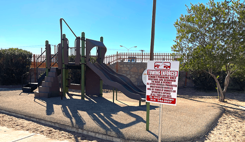 A sign in front of a playground warns that it is a towing enforced area.