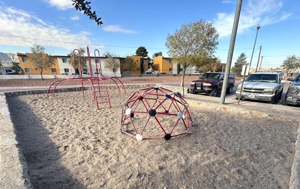 A playground with a red and white structure and a red swing set.