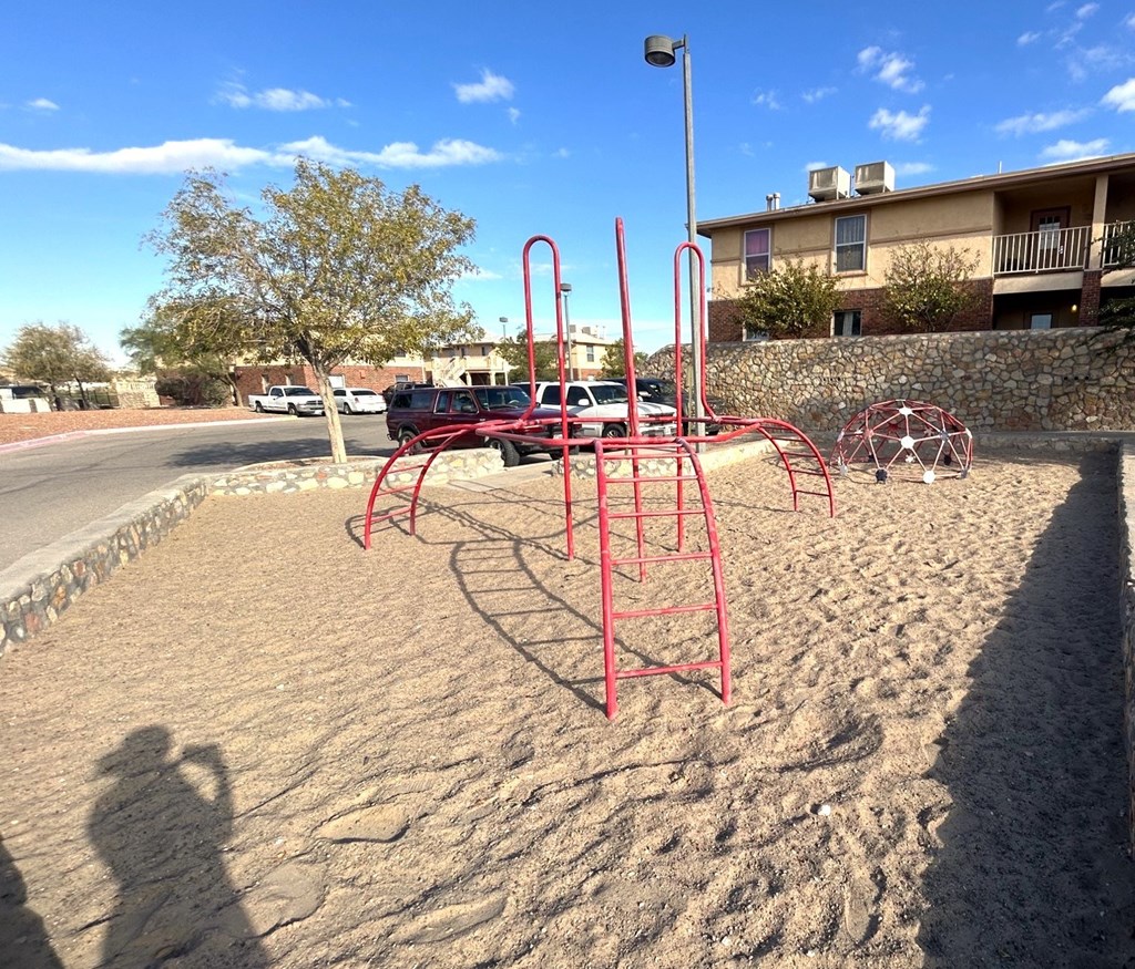 A playground with red equipment and a sandbox in the foreground.