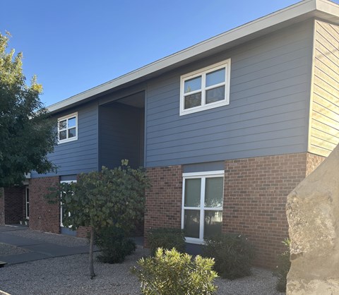 A grey house with a brick wall and a large rock in front.