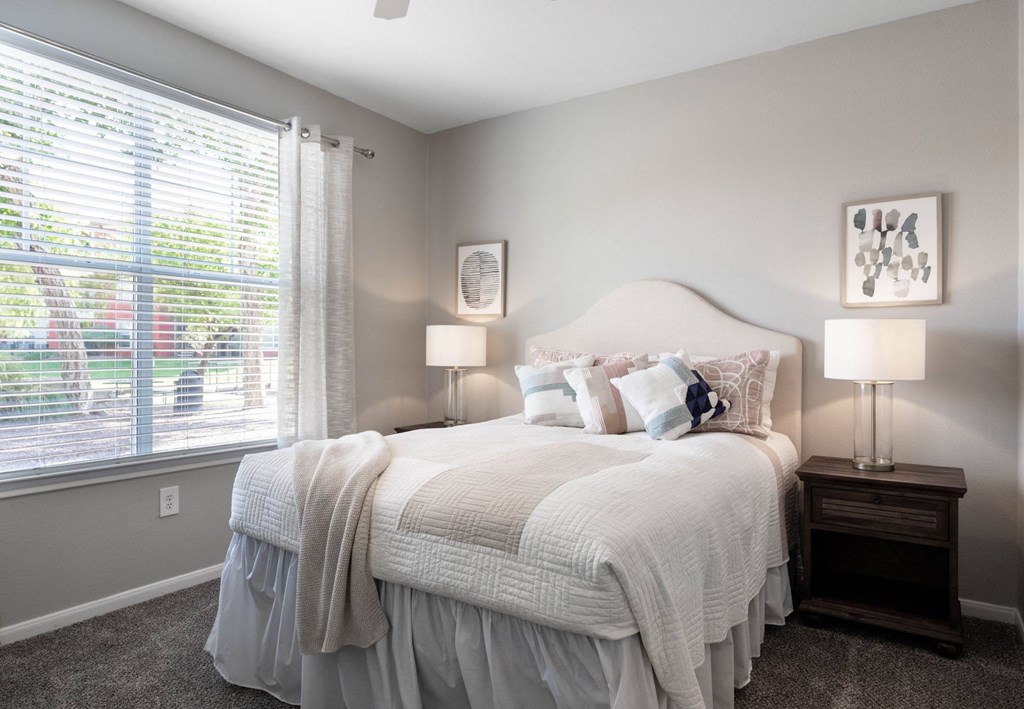 A bedroom with a large bed and a window with blinds.