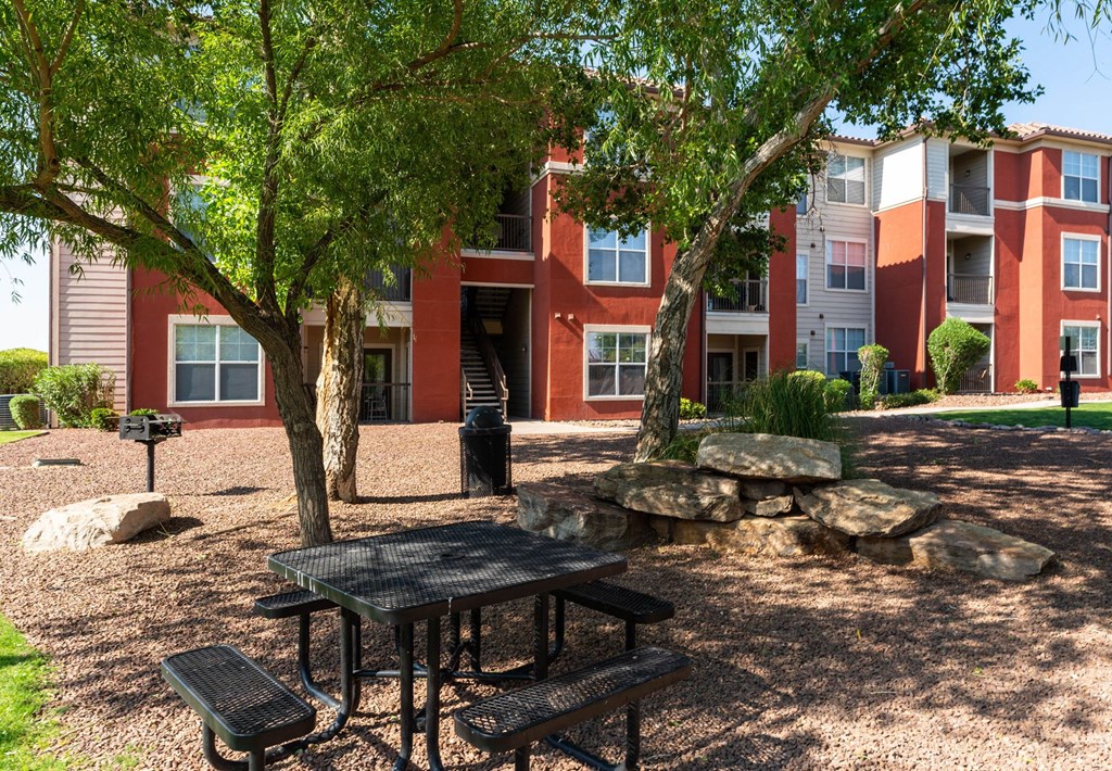A black table and benches are set up in a courtyard with a red building in the background.