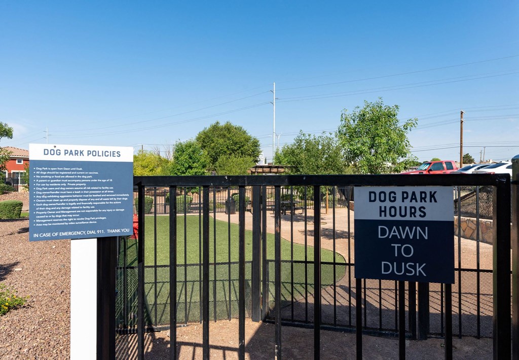 A sign at a dog park entrance states the park hours as dawn to dusk.