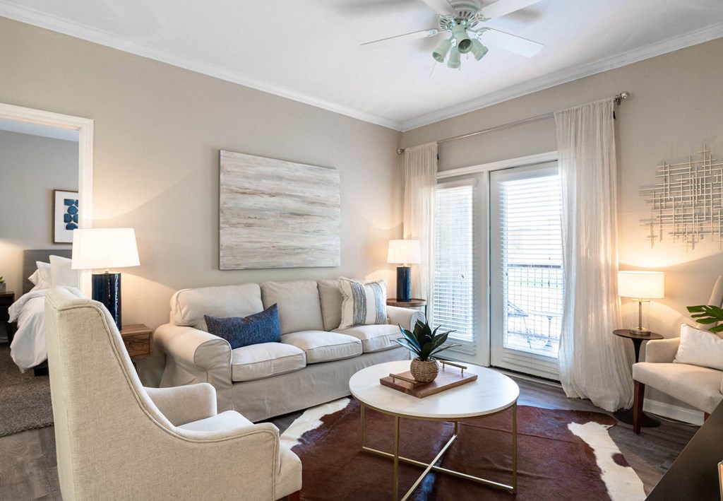 A living room with a white couch, a white chair, a white coffee table, a white rug, a white ceiling fan, a white wall, a white door, a white floor, a white table, a white lamp, a white