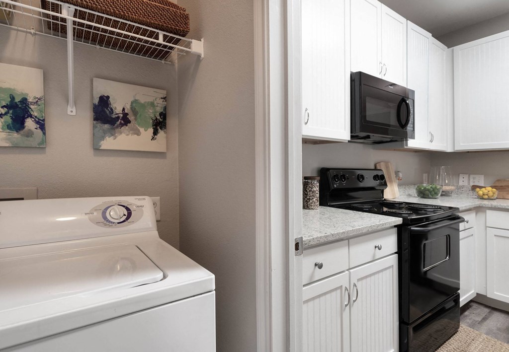A white washing machine is in a kitchen with white cabinets.