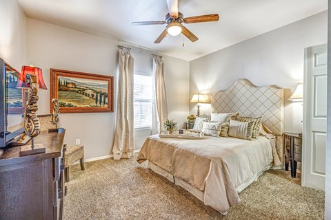 A bedroom with a bed, a ceiling fan, and a painting on the wall.