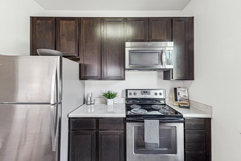 A modern kitchen with a stainless steel refrigerator, a stove with an oven, and dark brown cabinets.