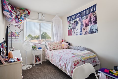 A bedroom with a bed, desk, and a wall with a "Happy Birthday" poster.
