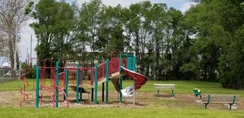 A playground with a red and green slide and a green bench.