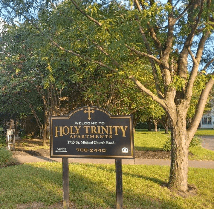 a sign for holy trinity apartments in front of a tree