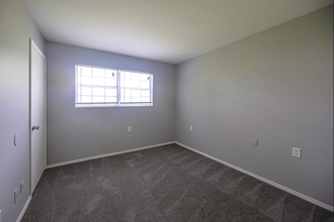 an empty bedroom with a window and carpeting