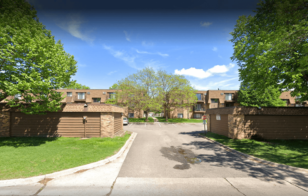 Inviting brick apartment complex with mature trees and private garages on a sunny day.