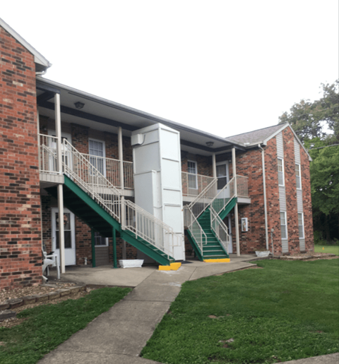 A brick building with a white door and a green staircase.