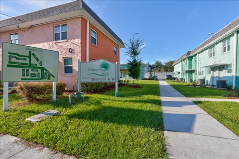 A sign for Polkline Gardens is in front of a pink building.
