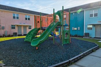 A playground with a green slide in the middle of a gravel area.