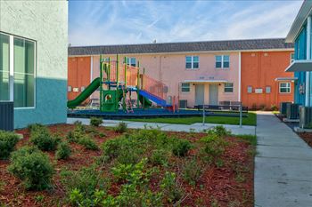 A playground with a green slide and red mulch in the foreground.