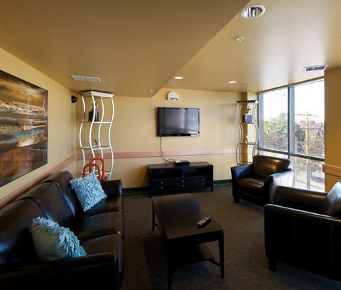 A living room with a brown leather couch, a black coffee table, and a television mounted on the wall.