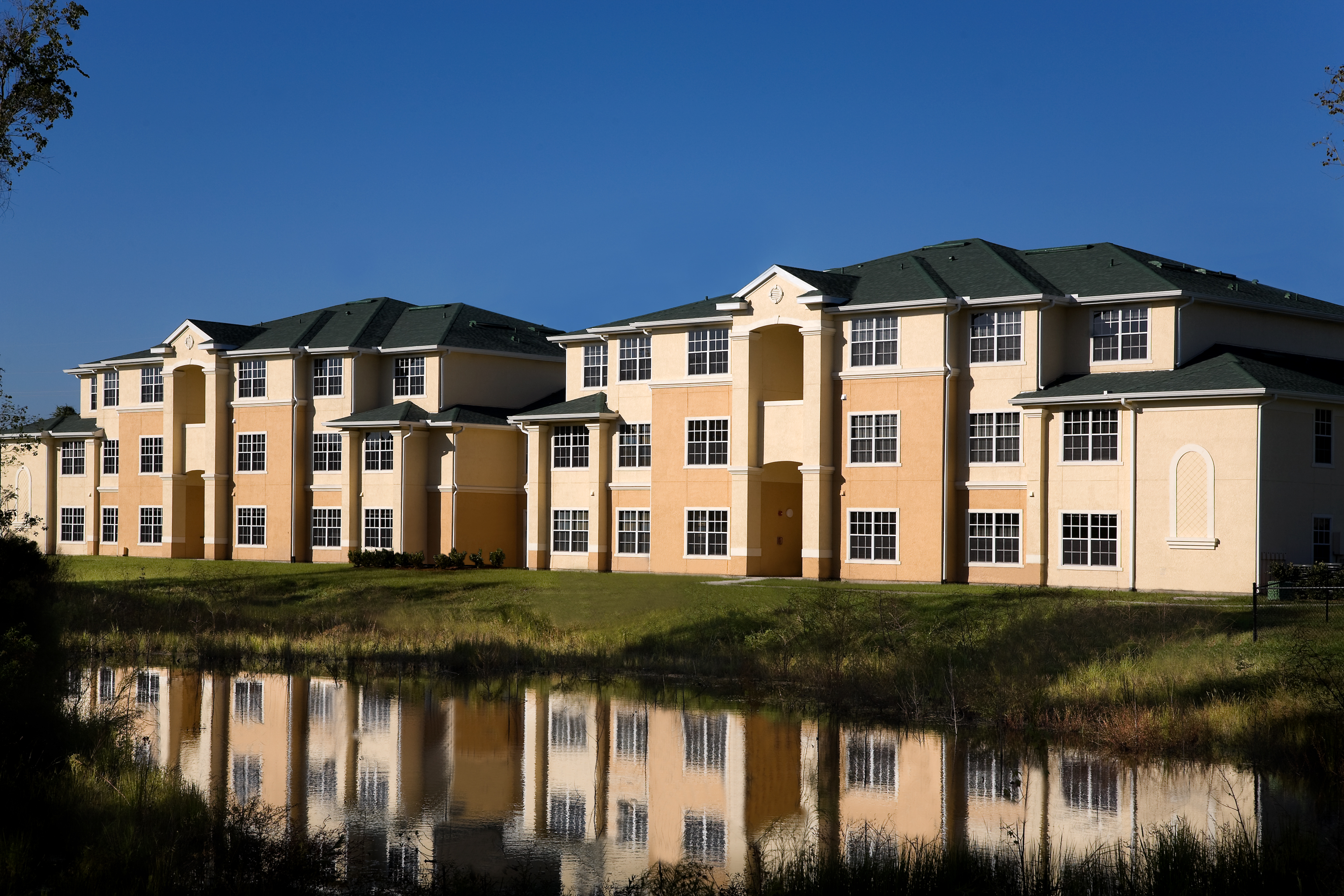 A large building with a green roof is reflected in the water in front of it.