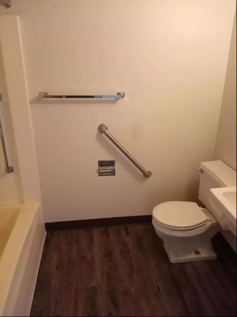 A white toilet with a silver grab bar mounted on the wall.