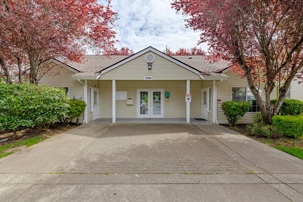 the front of a white house with a driveway and trees