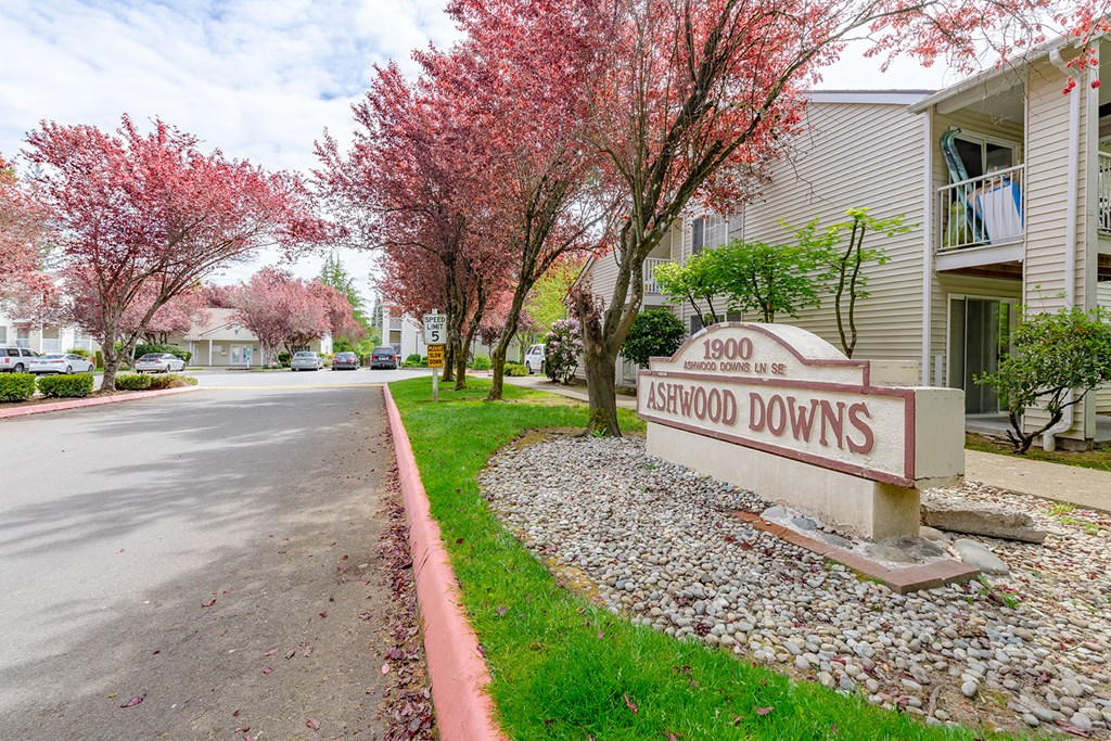 a street sign in front of apartments with pink blossoming trees