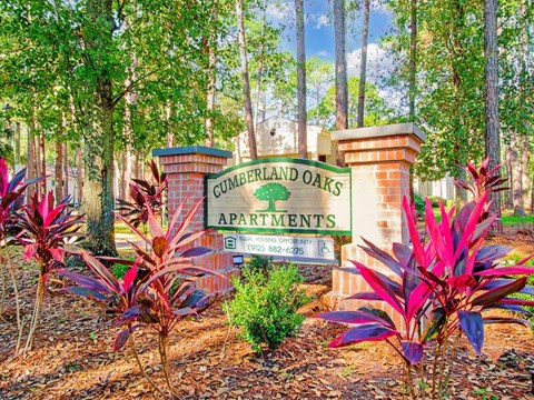 A sign for Cumberland Oaks Apartments is surrounded by plants.