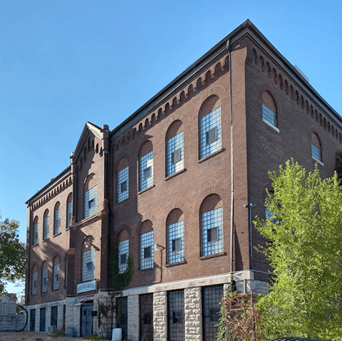 A large red brick building with many windows and a tree in front.