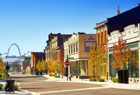 A city street with a stop sign and a large arch in the background.
