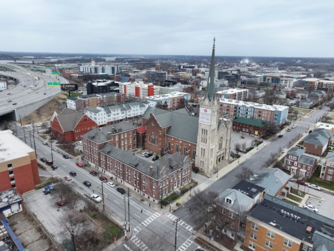 A church with a tall steeple is in the middle of a city intersection.