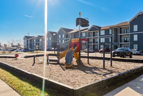 A playground with a yellow slide in front of apartment buildings.