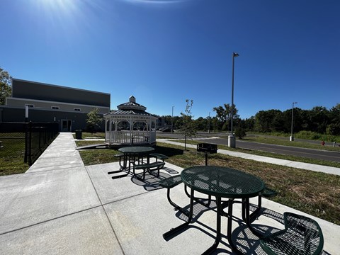 A sunny day at a park with picnic tables and a gazebo.