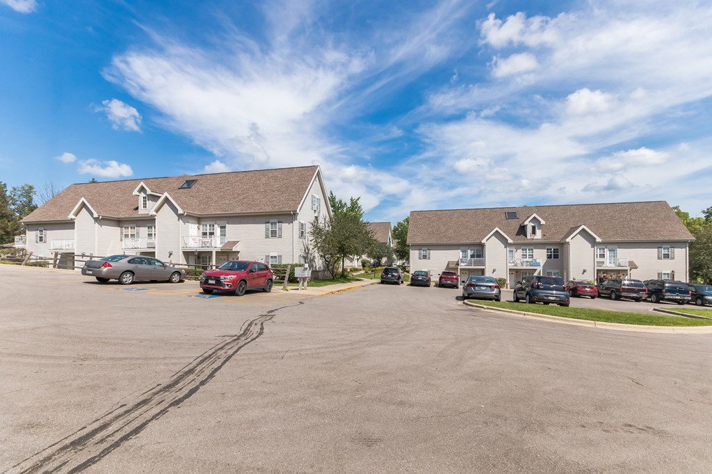 A parking lot with cars and two buildings in the background.