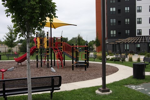 A playground with a yellow umbrella and a red slide.