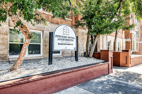 A sign for Stevens-Duval Apartments stands in front of a brick building.
