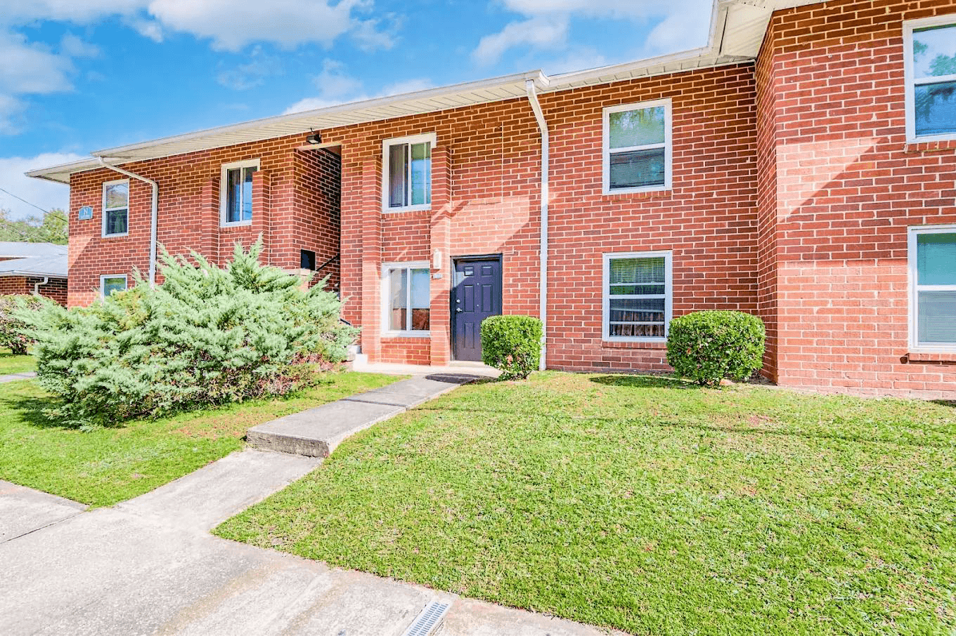 A red brick apartment building with a green lawn in front.