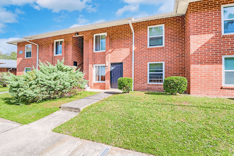 A red brick apartment building with a green lawn in front.