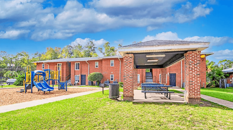A playground with a slide and a bench in front of a brick building.