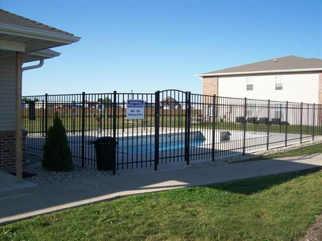 A black fence surrounds a pool and a house.