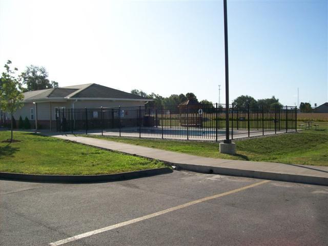 A building is behind a black fence and there is a pole in the foreground.