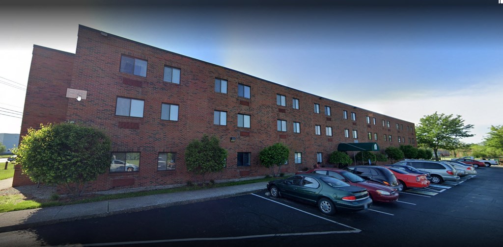 Three-story brick apartment building with a front parking lot and green awning at the entrance