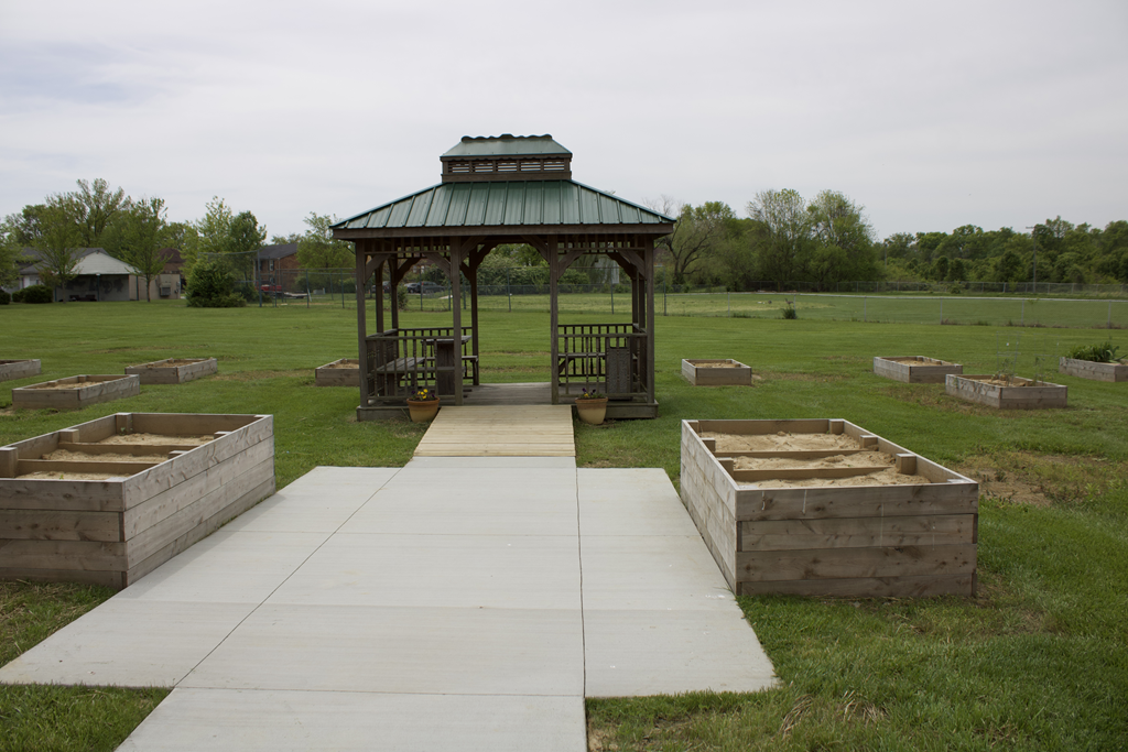 Wooden gazebo surrounded by raised garden beds in a grassy outdoor area