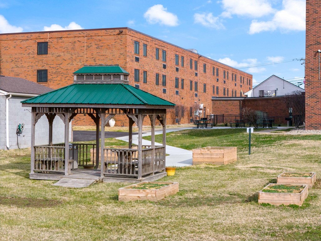 Wooden gazebo and raised garden beds in courtyard near brick apartment buildings