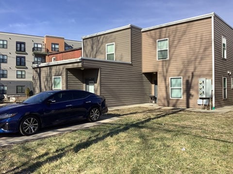 A blue car is parked in front of a modern two-story building.