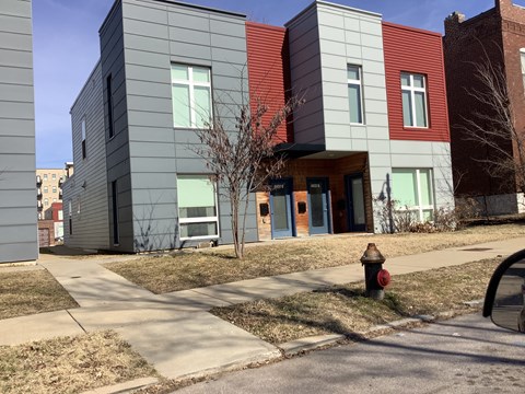 A fire hydrant is in front of a grey building with a red door.
